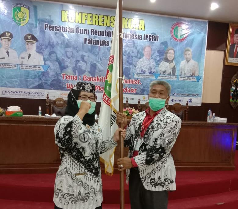 Ernawaty, Ketua PGRI Kota Palangka Raya Periode 2016-2021 saat menyerahkan bendera organisasi PGRI kepada Sujianto selaku ketua PGRI kota Palangka Raya terpilih periode 2020-2025, Rabu (23/12/2020). Foto : AT