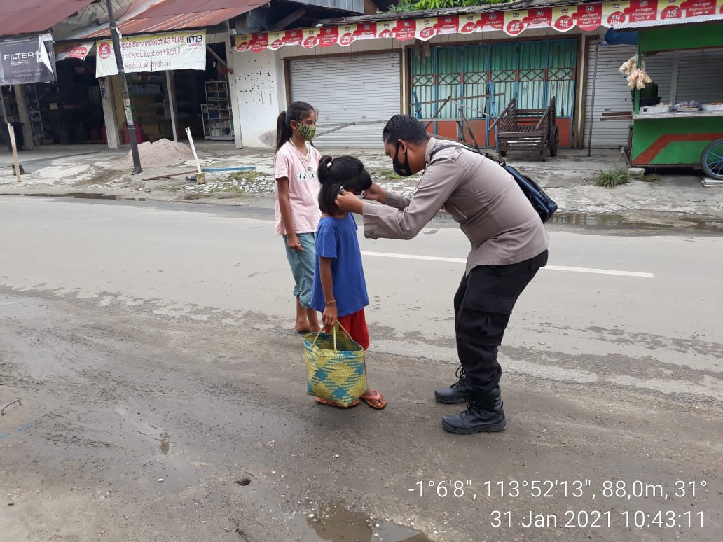 Anggota Polres Gumas saat membantu memakaikan masker yang benar kepada seorang anak di Kota Kuala Kurun Gumas. FOTO : tbn.